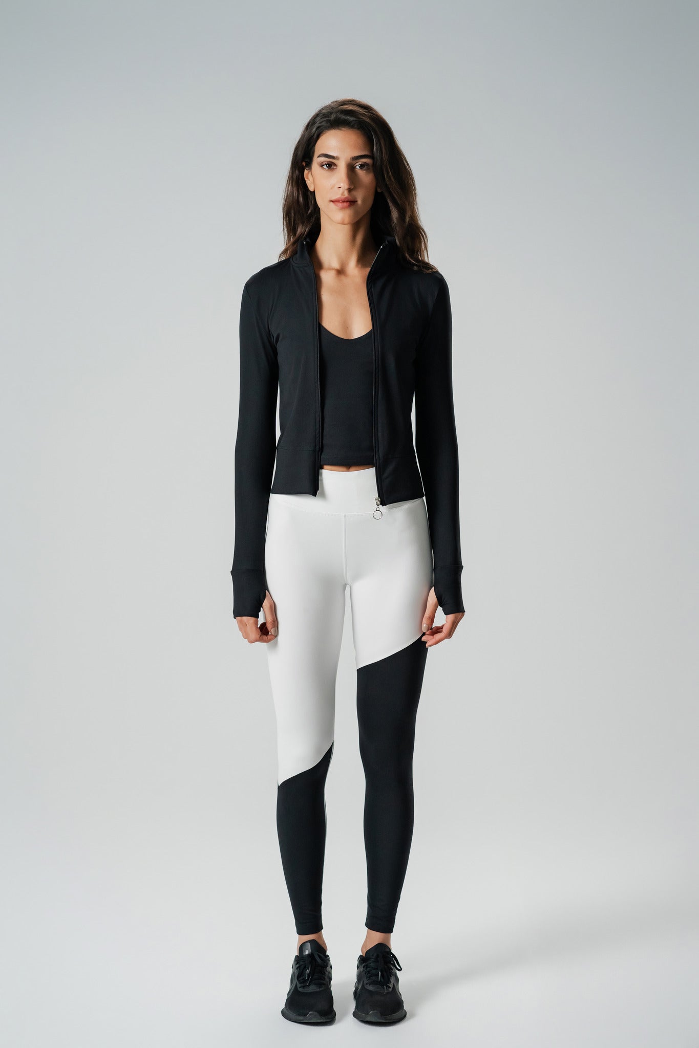 A woman wearing a black zip-up sports jacket paired with white & black Leggings.