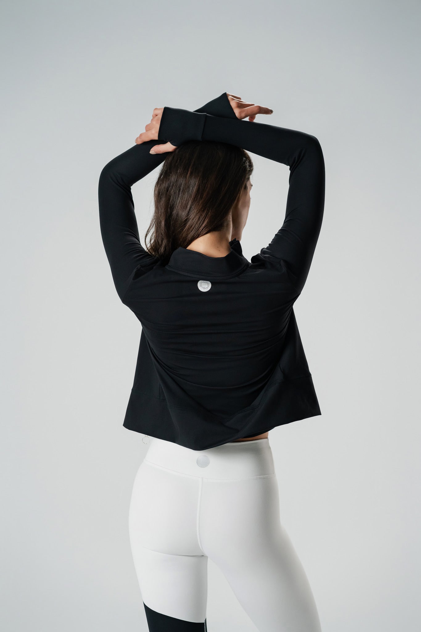 A woman wearing a black zip-up sports jacket giving us her back paired with white athletic pants.