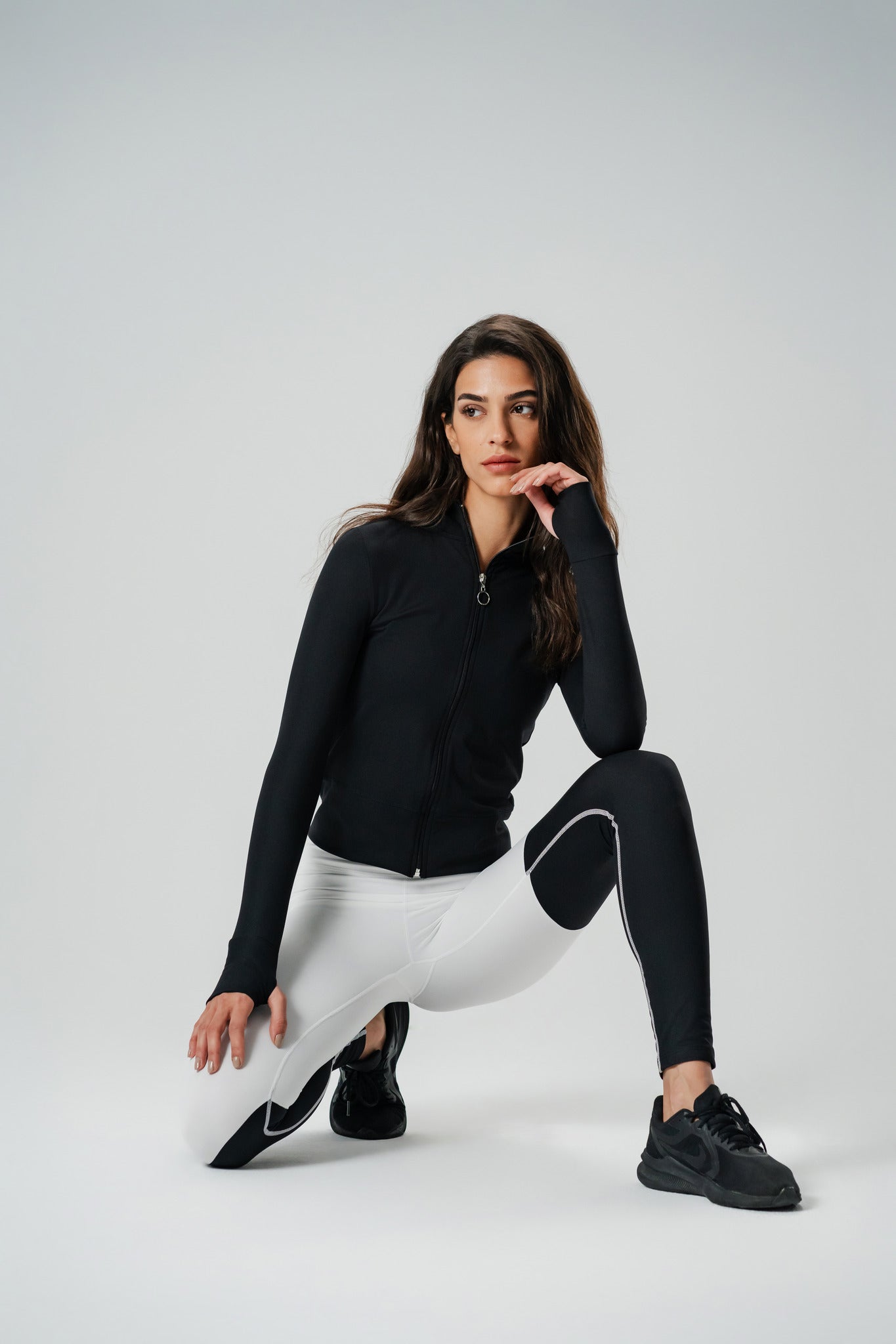 A model posing in black zip-up sports jacket paired with white & black athletic pants.