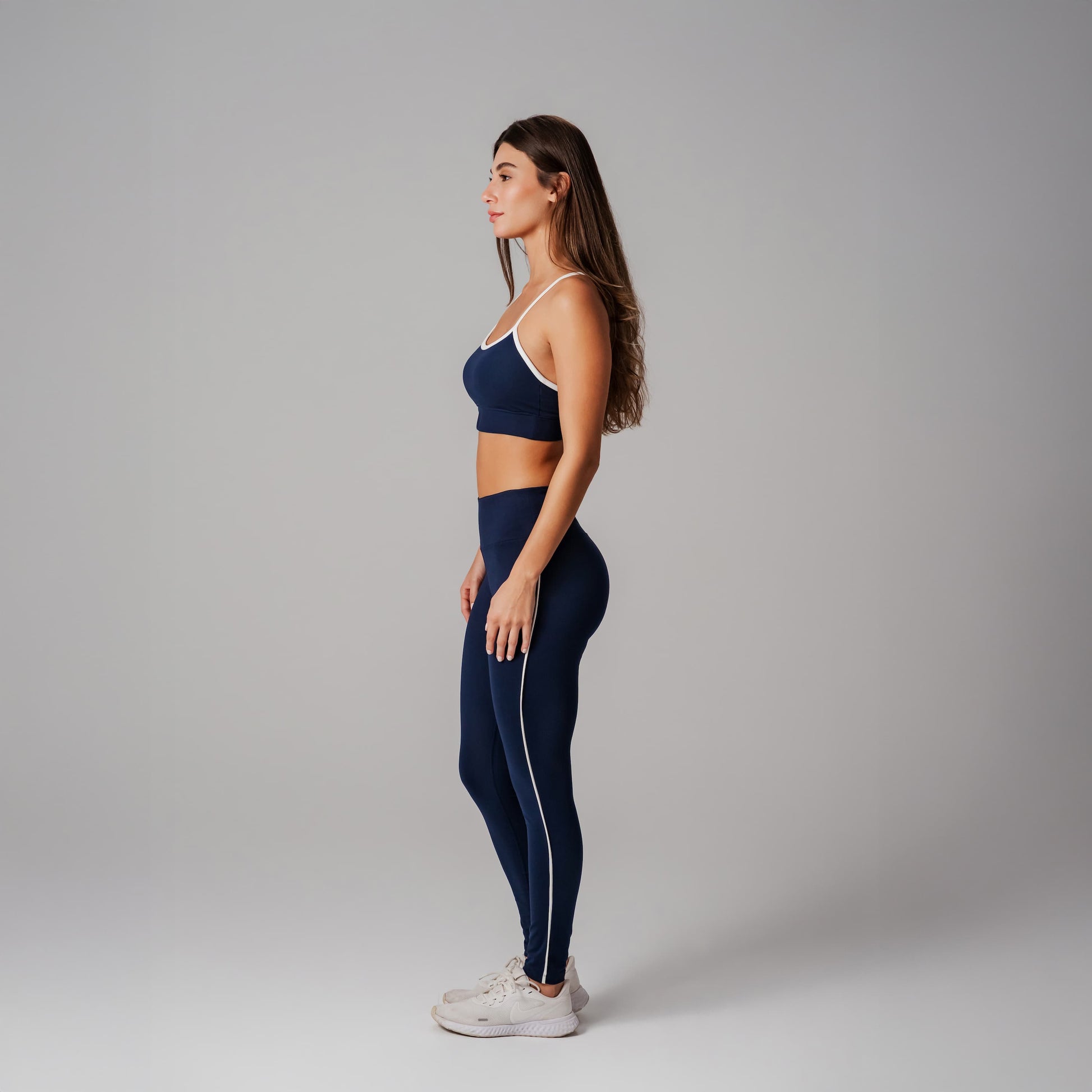 Woman wearing a navy blue sports bra and leggings set on a gray background
