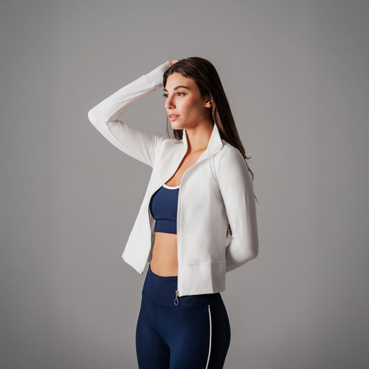 Woman wearing a white jacket over a blue sports bra and leggings on a gray background