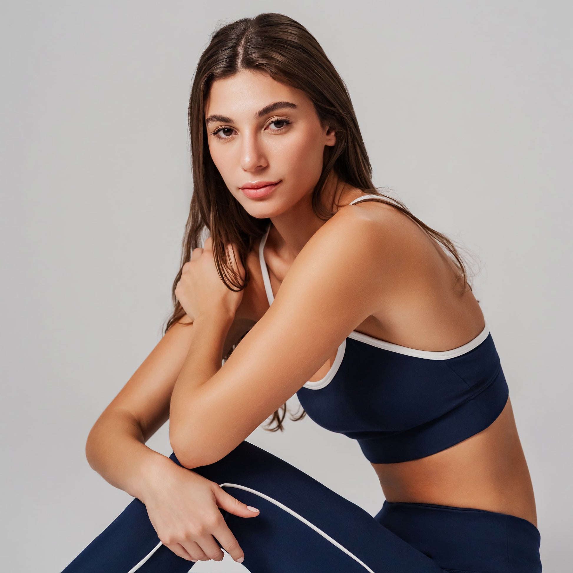 Sports model wearing a navy sports bra and leggings against a gray background