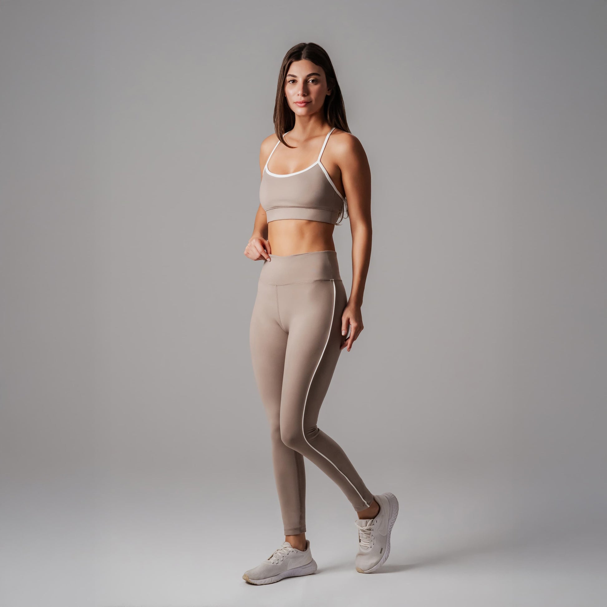 Woman wearing a beige sports bra and leggings set on a gray background