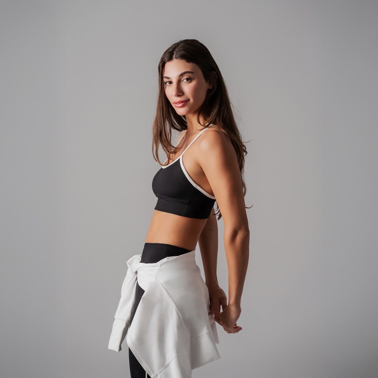 Woman wearing a black sports bra and white skirt against a gray background