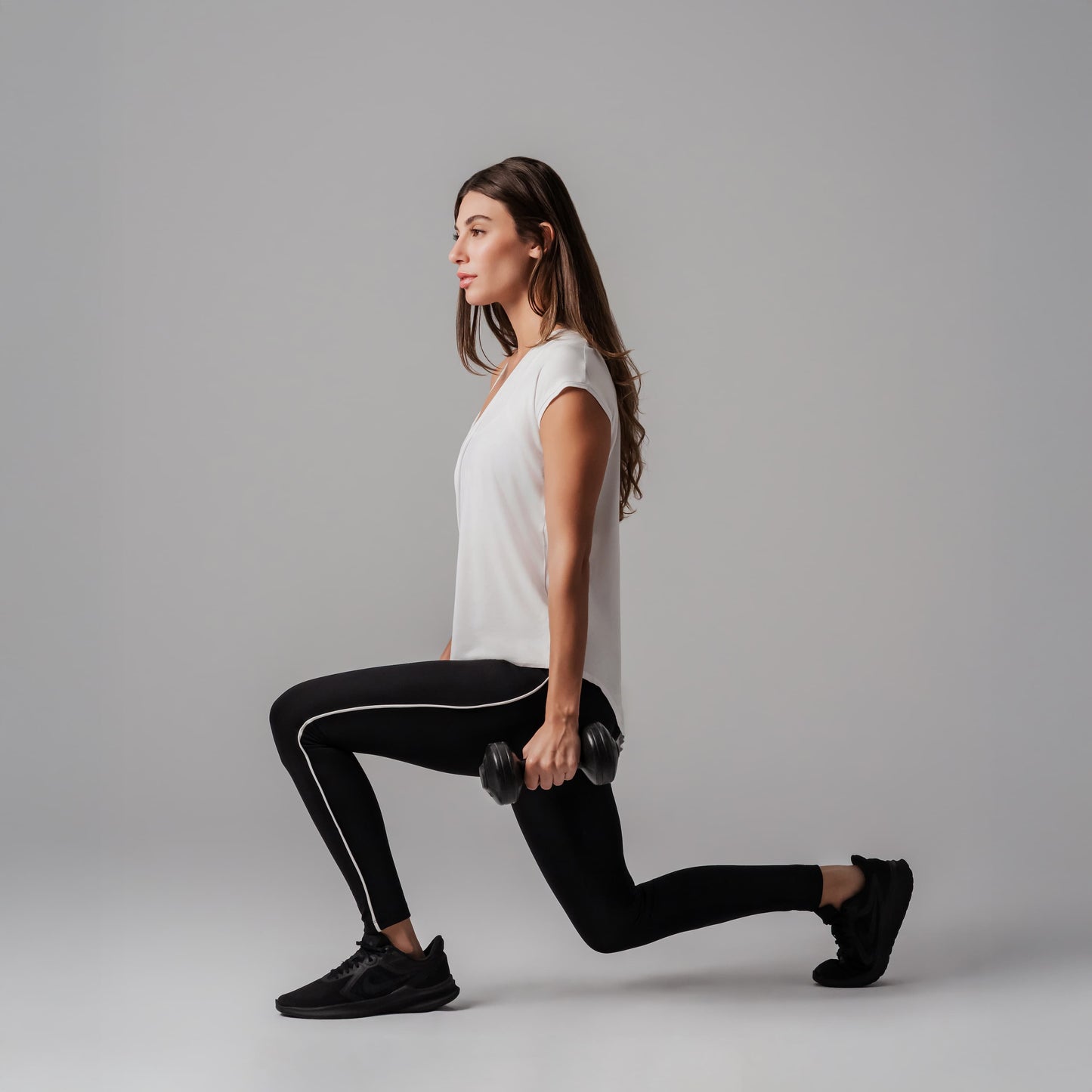 Woman performing lunges with dumbbells on a gray background