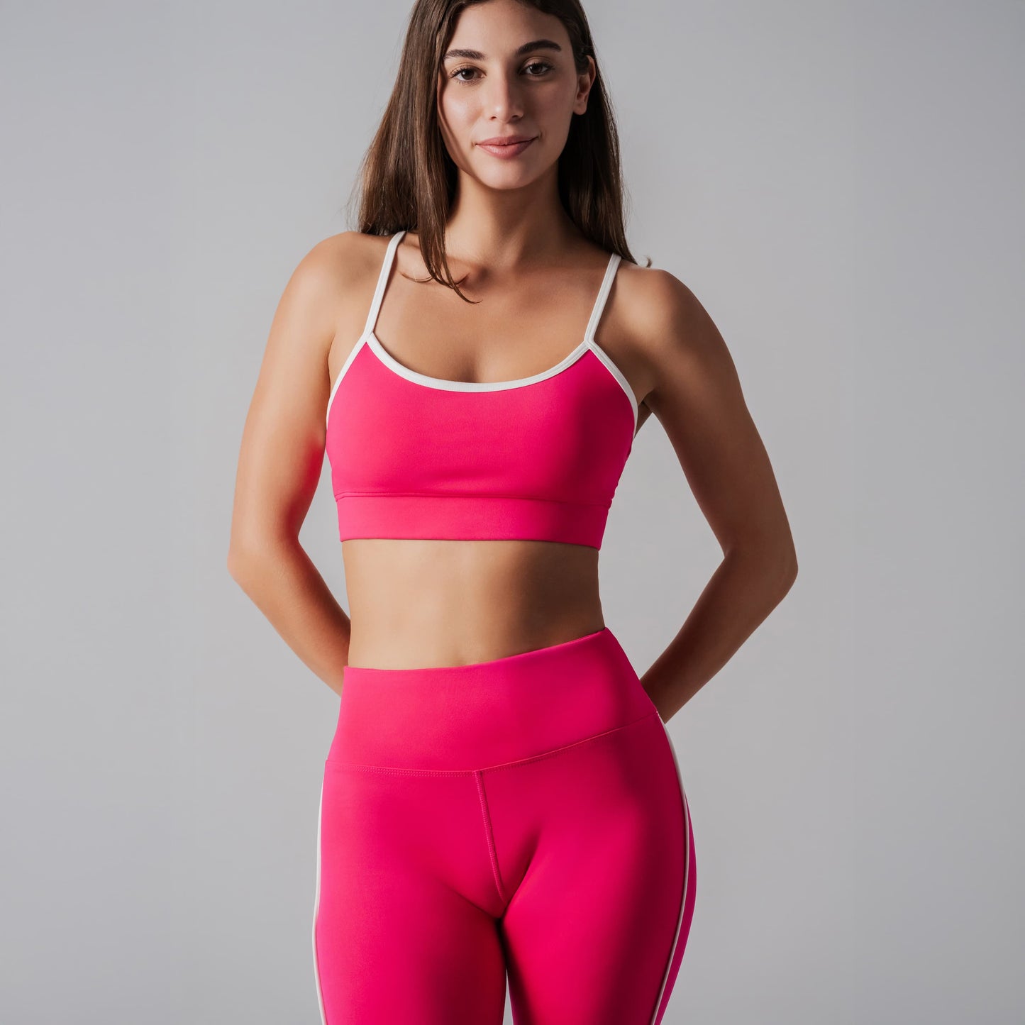 Woman wearing a bright pink sports bra and leggings on a gray background