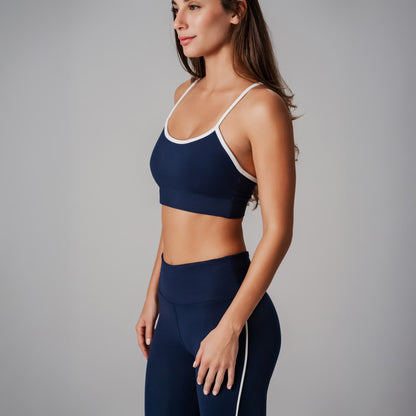 A model wearing a navy blue sports bra and leggings with white trim on a gray background