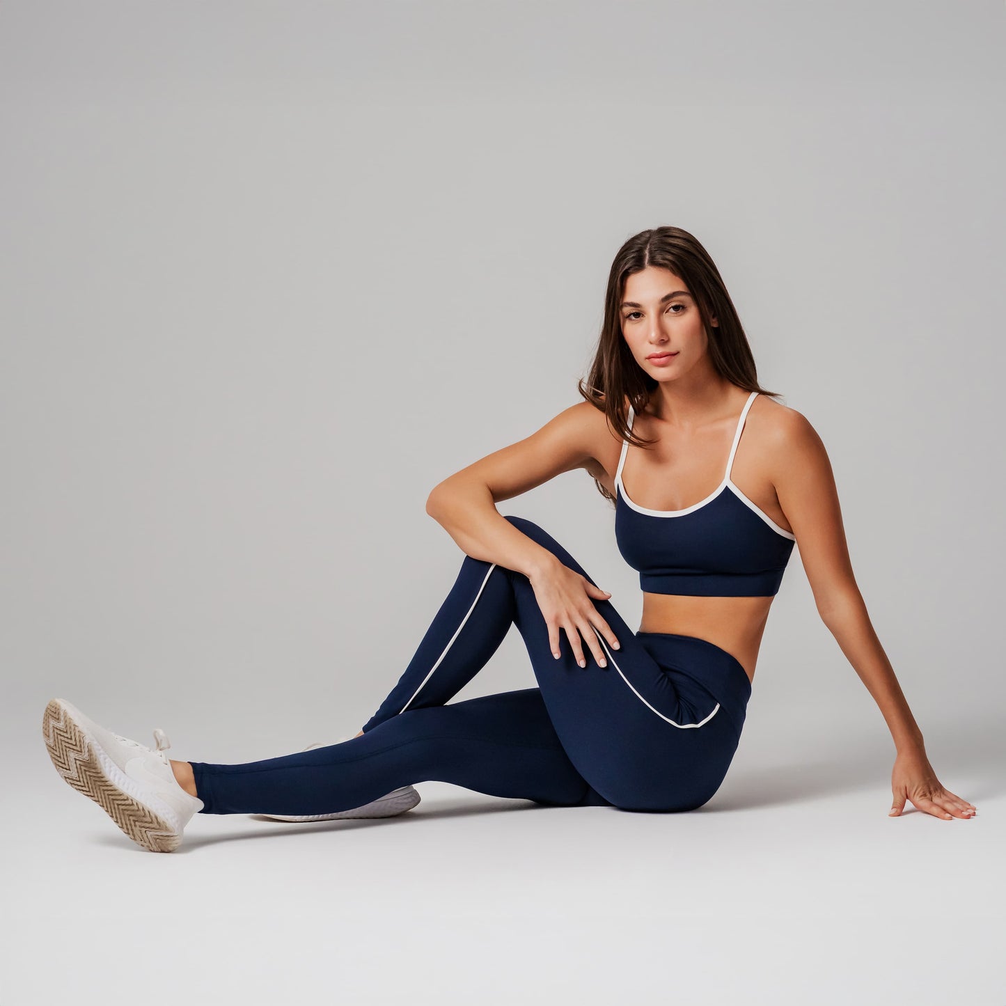 Woman in navy sports bra and leggings sitting on a light gray background