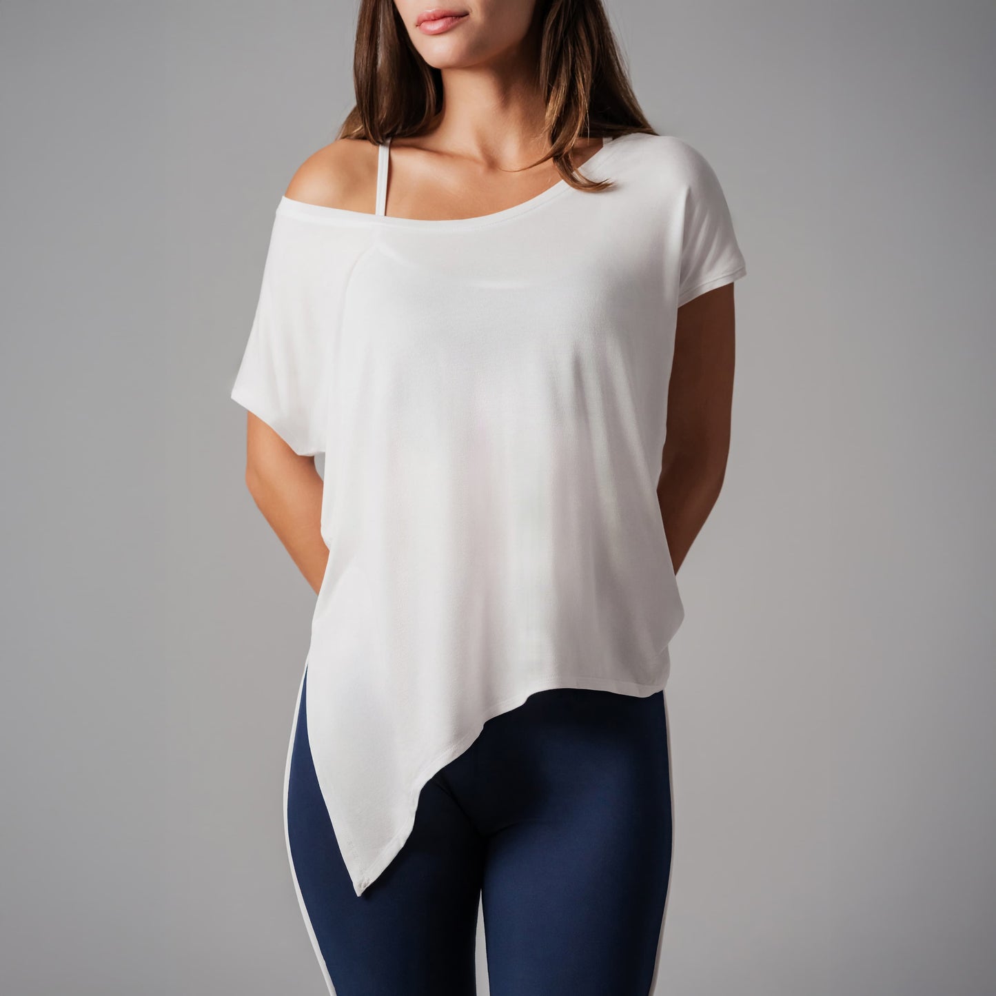 Woman wearing a white off-shoulder top and dark blue leggings on a gray background