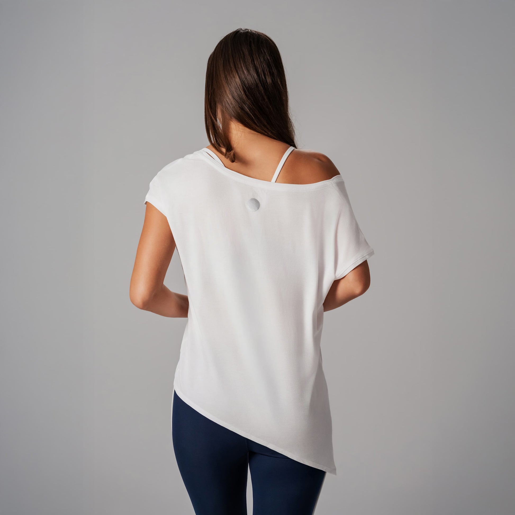 A model wearing a white off-shoulder top and dark blue pants on a gray background