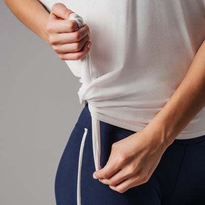 Fitness model wearing a white top and navy pants with a gray background