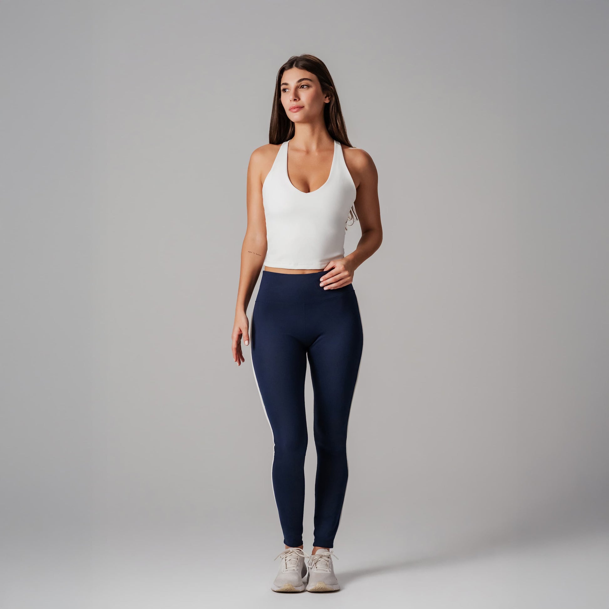 Woman wearing a white tank top and navy leggings on a gray background