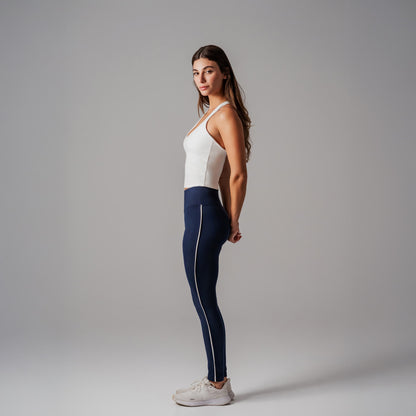 Woman wearing a white tank top and navy leggings with a white stripe on a gray background