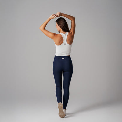 Model wearing a white sports bra and navy leggings on a gray background