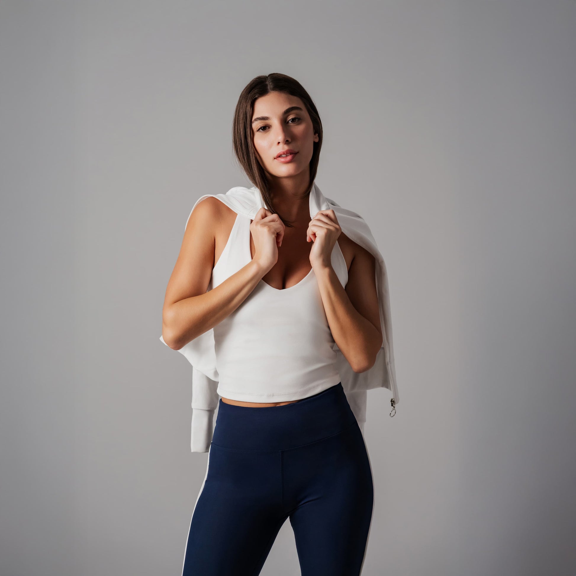 Woman in athletic wear holding a jacket against a gray background