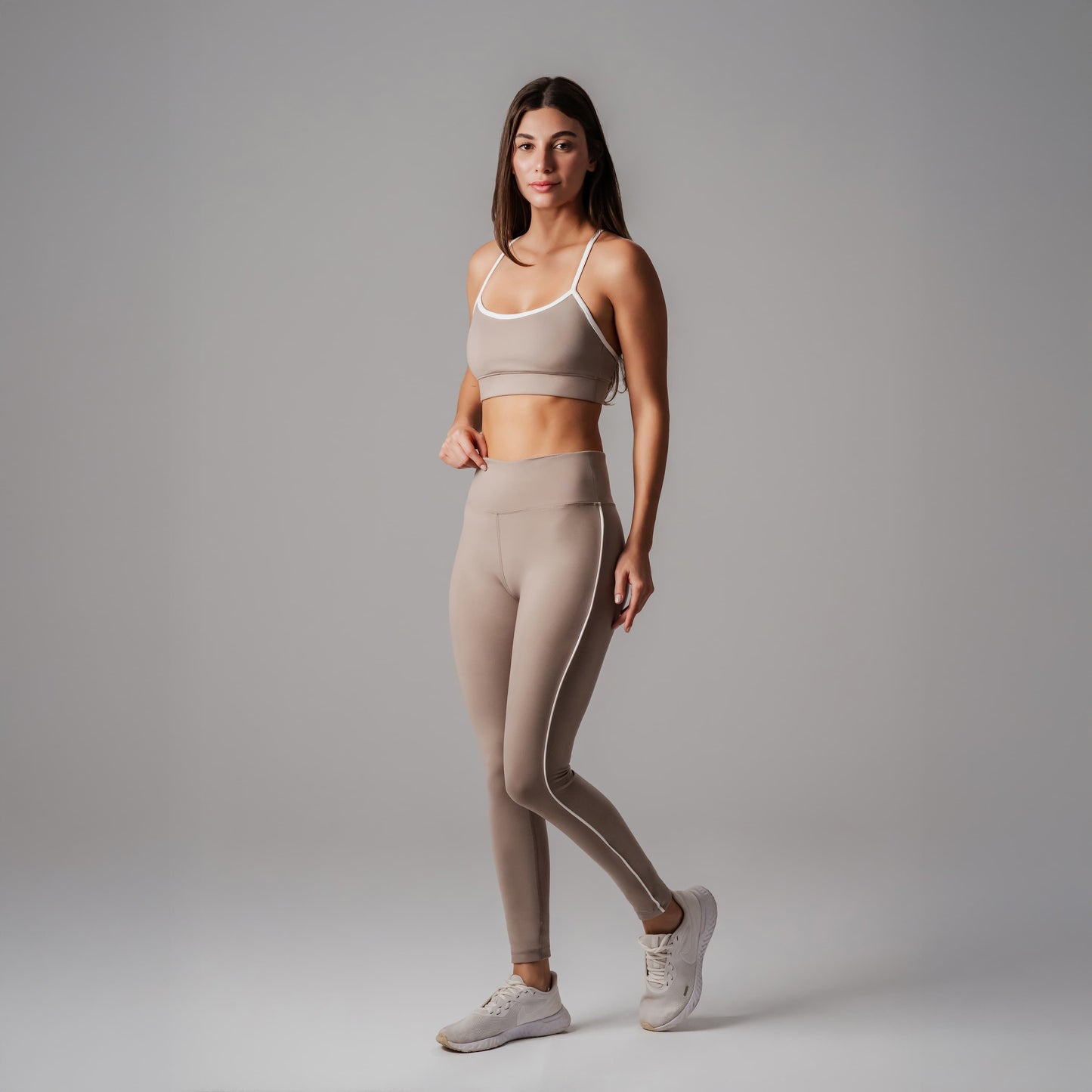 Woman wearing a beige sports bra and leggings set on a gray background