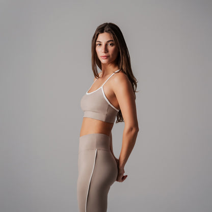 Woman wearing a beige sports bra and leggings on a gray background