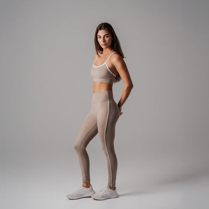 Woman wearing a beige sports bra and leggings set on a gray background