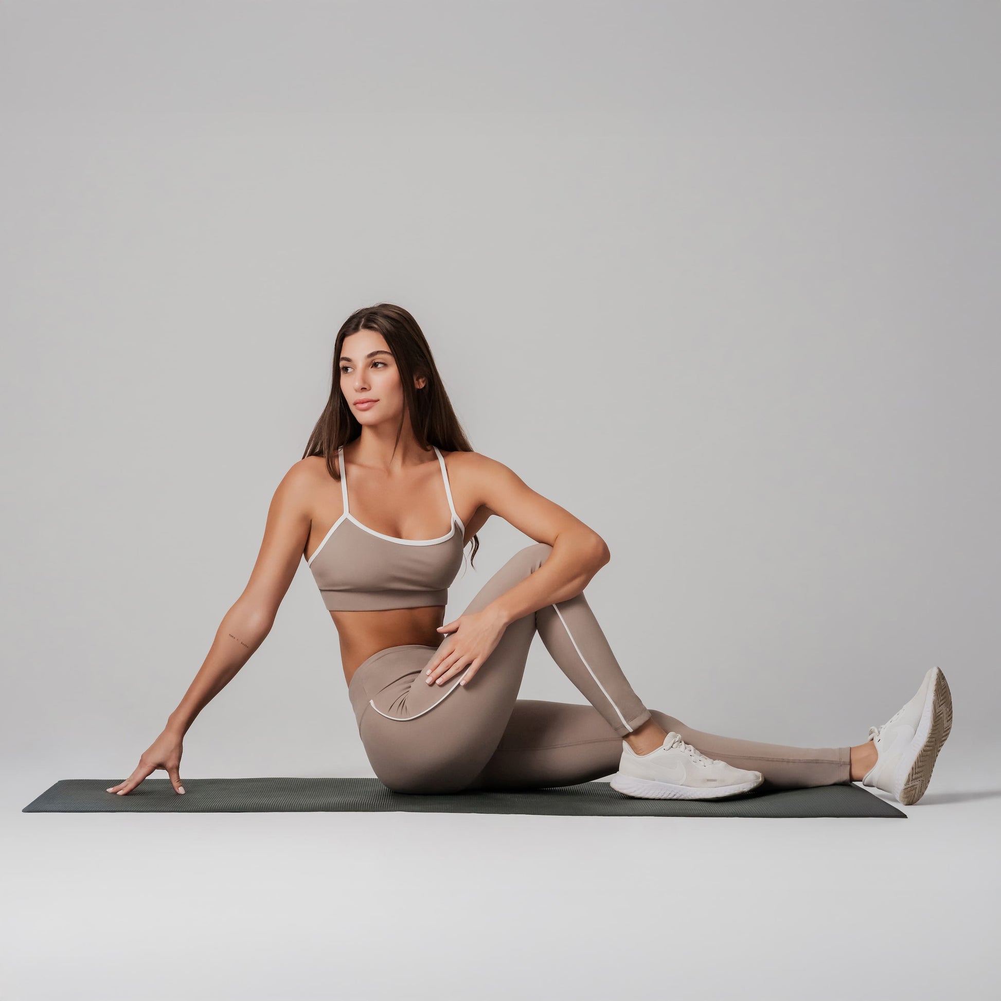 Woman in beige athletic wear stretching on a mat against a plain background