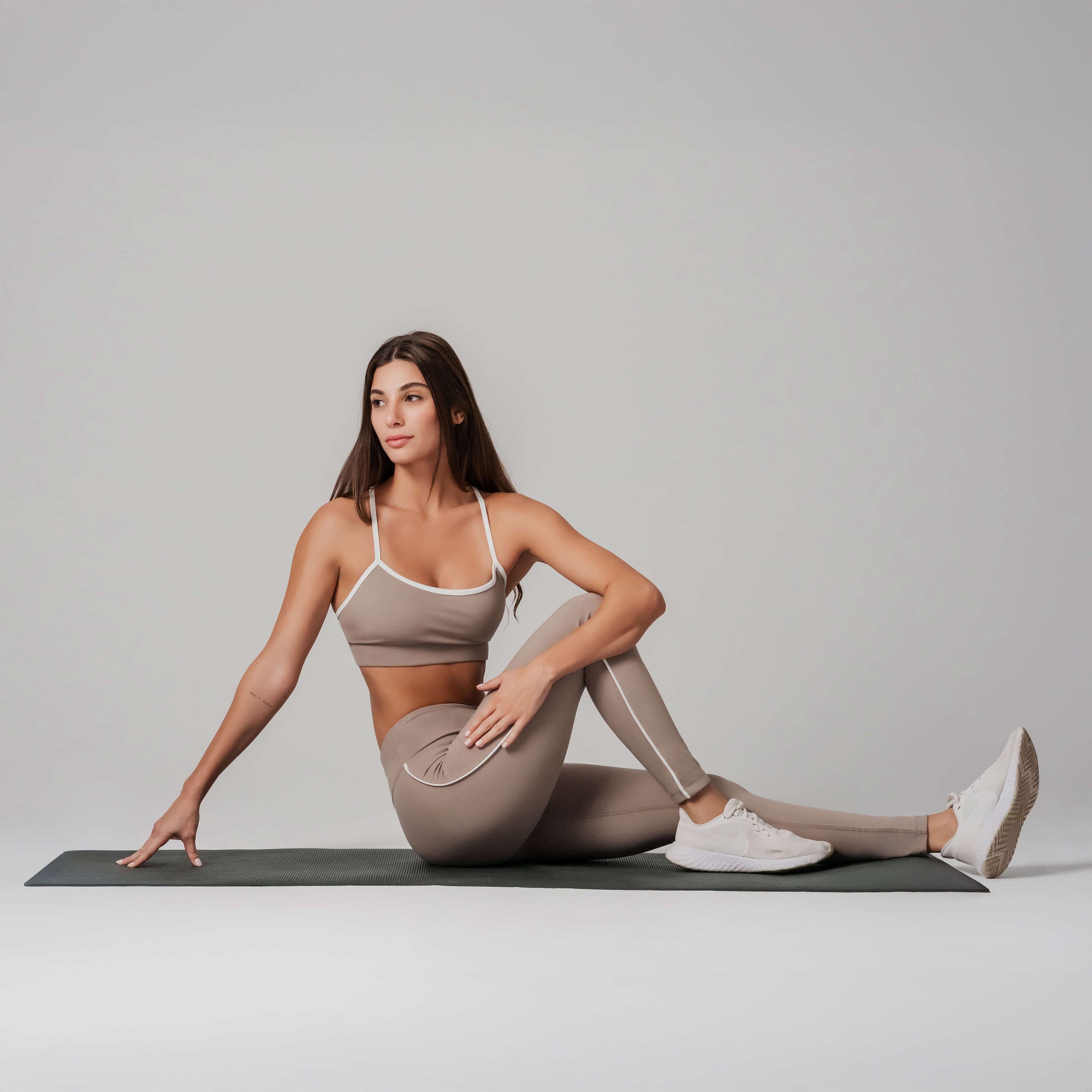 Woman in beige athletic wear stretching on a mat against a plain background