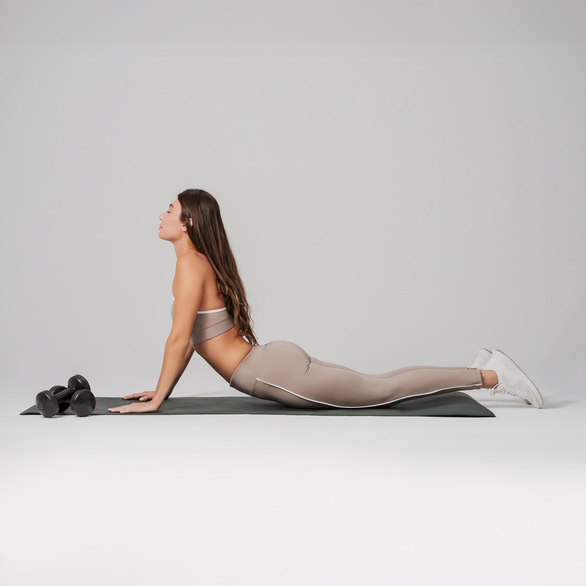 Woman in a yoga pose on a mat with a gray background