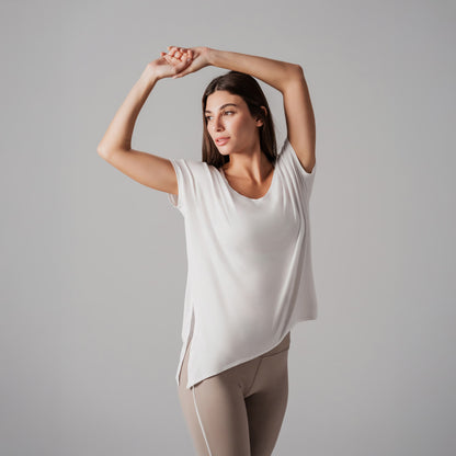 Woman wearing a white sleeveless top and beige leggings against a gray background