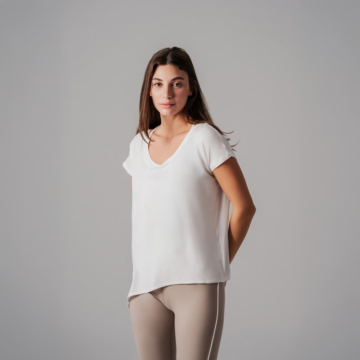 Woman wearing a white t-shirt and beige pants against a gray background