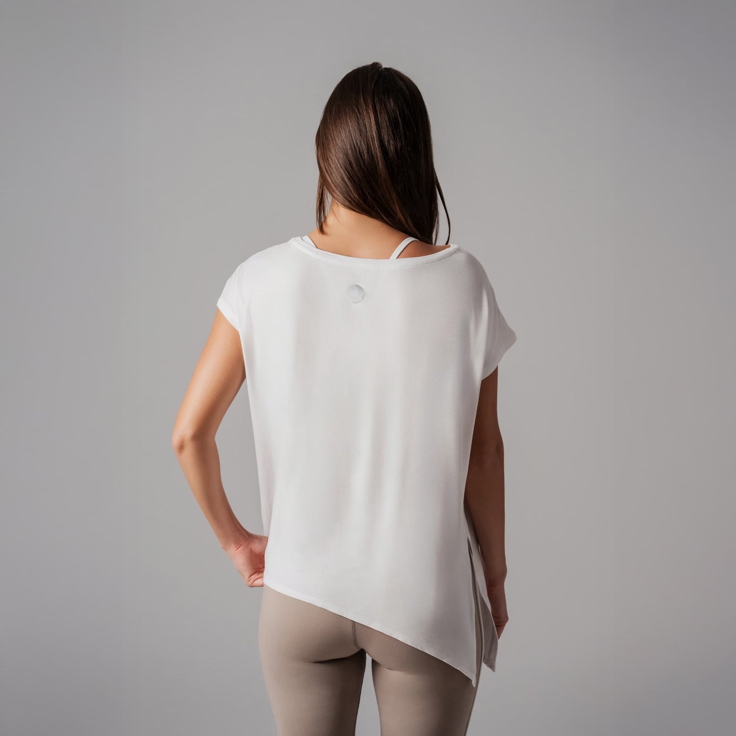 Woman wearing a white sleeveless top and beige pants against a gray background