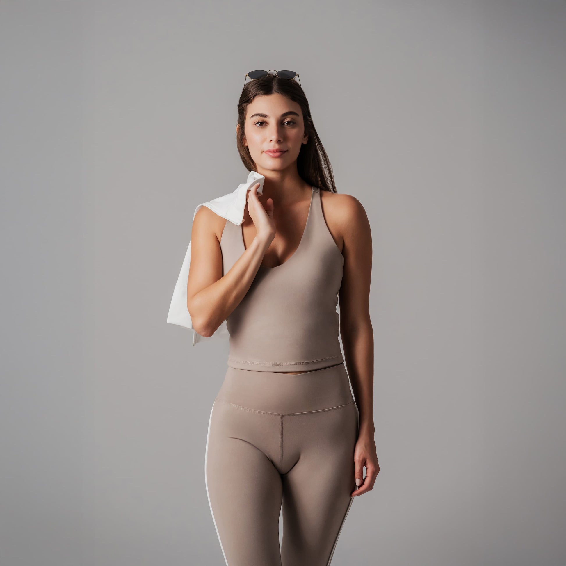 Woman in beige athletic wear holding a white jacket against a gray background