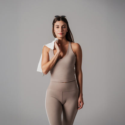 Woman in beige athletic wear holding a white jacket against a gray background