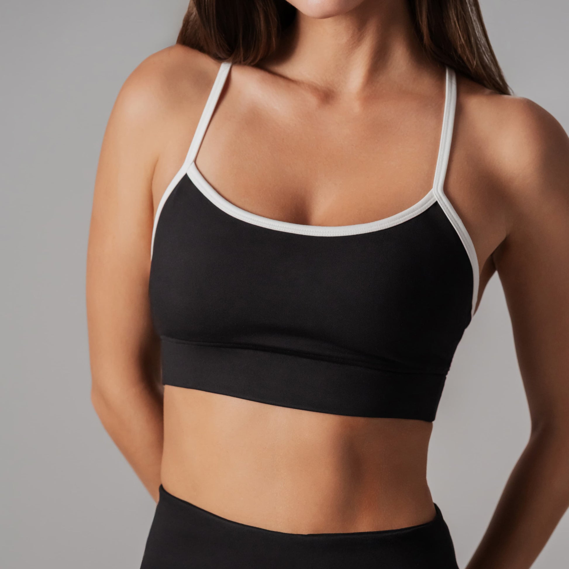 Black sports bra with white straps worn by a person on a gray background