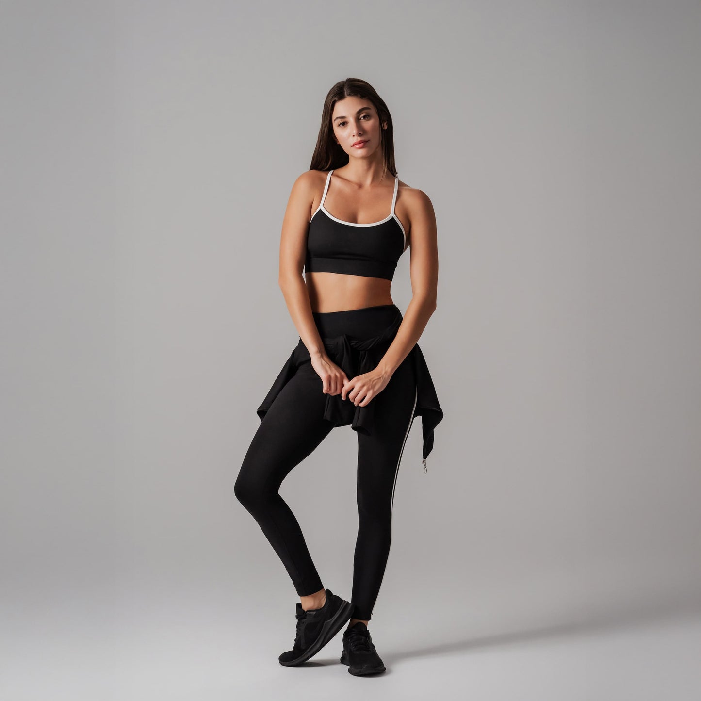 Woman wearing a black sports bra and leggings on a gray background