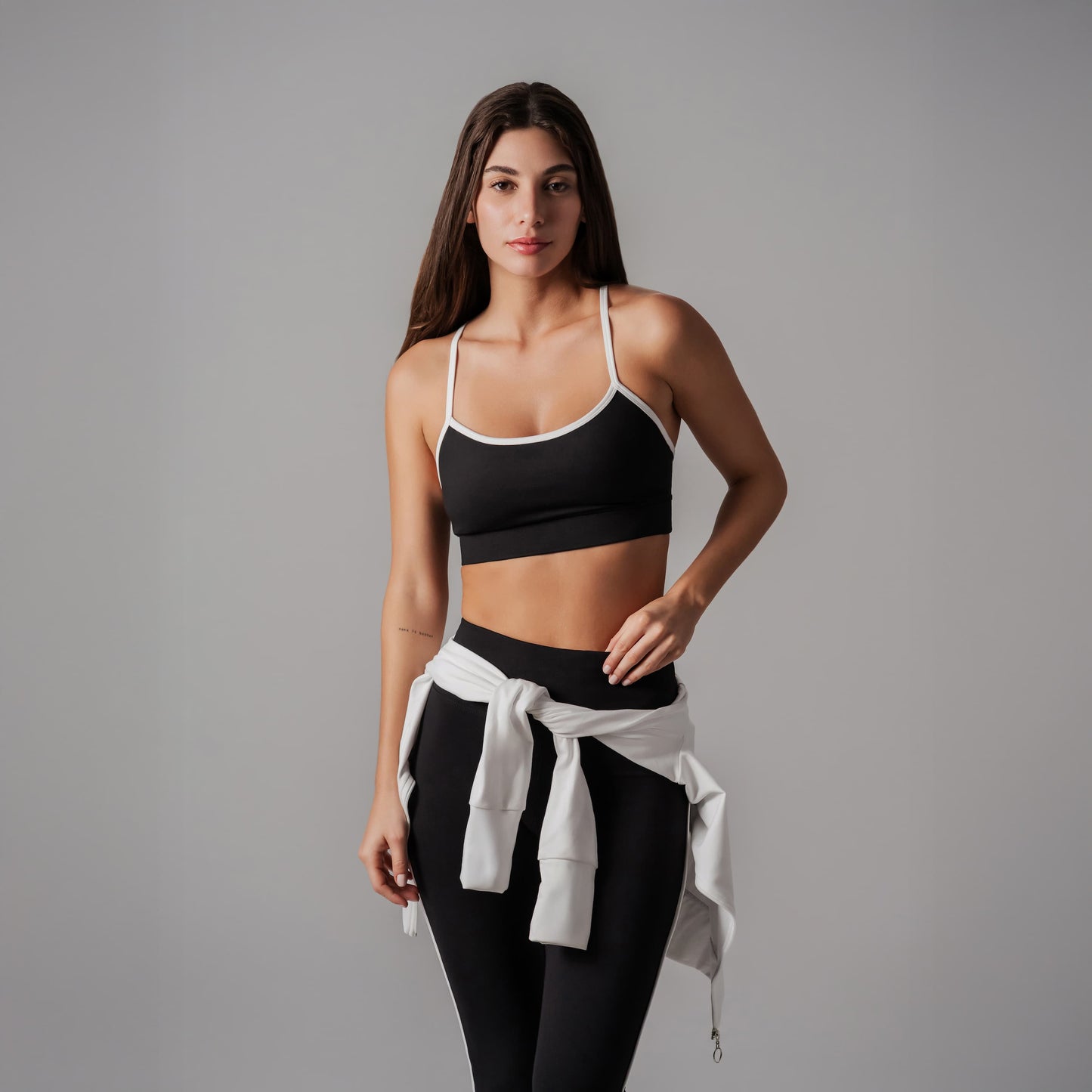 Woman wearing a black sports bra and leggings with a white towel on a gray background