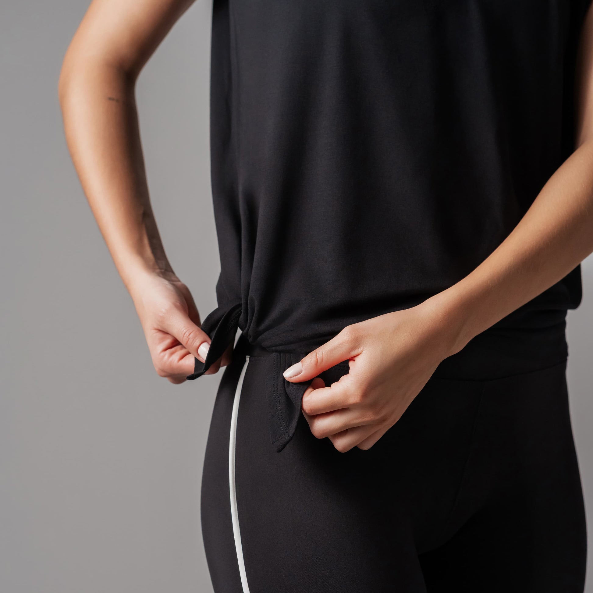 Person adjusting a black sleeveless top against a gray background
