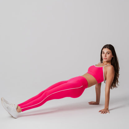 Woman in fuchsia athletic wear performing a plank on a light gray background