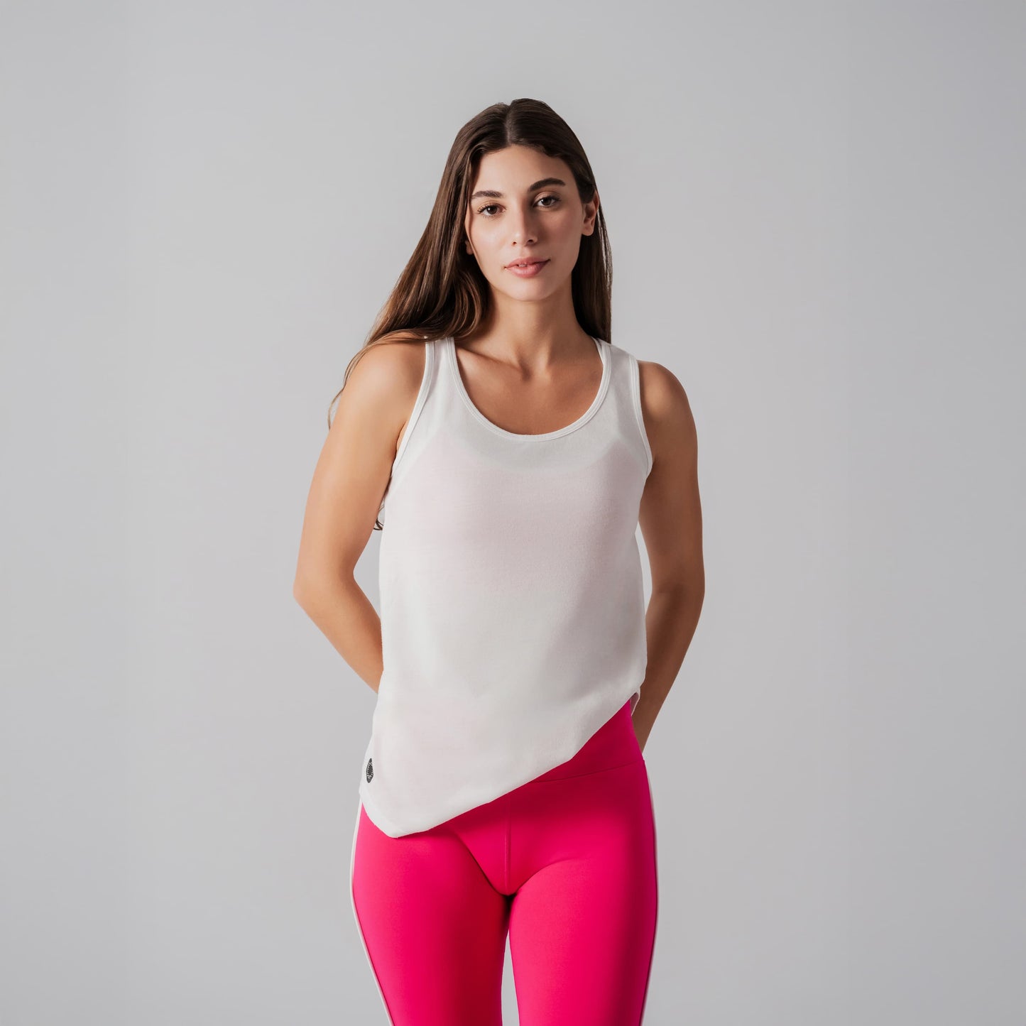 Woman wearing a white tank top and pink leggings against a gray background