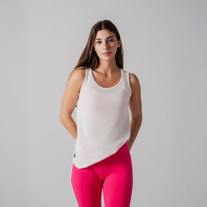 Woman wearing a white tank top and pink leggings against a gray background