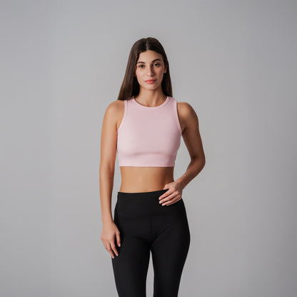 Woman wearing a pink cropped ribbed tank and black leggings on a gray background