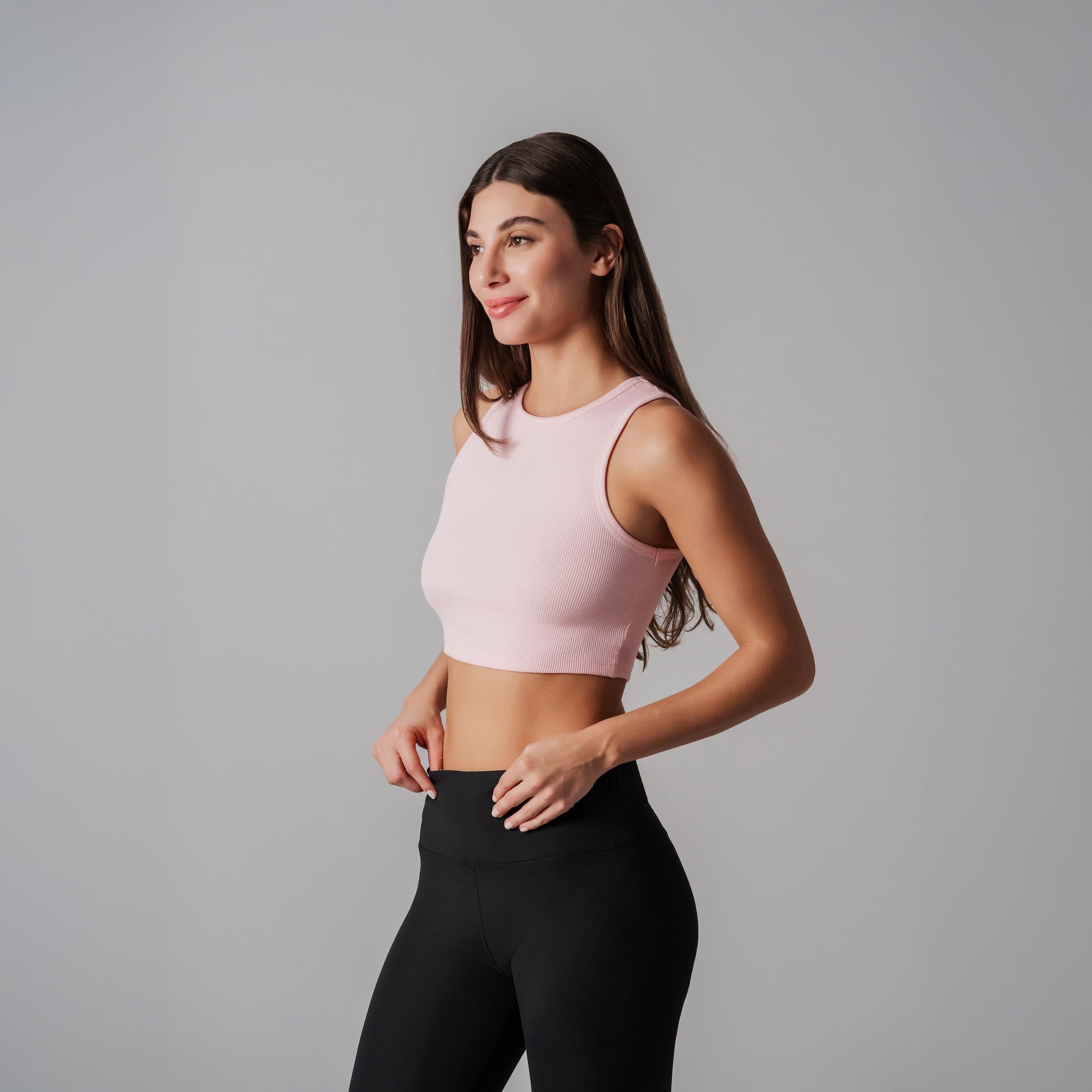 Woman wearing a pink cropped tank and black leggings on a gray background