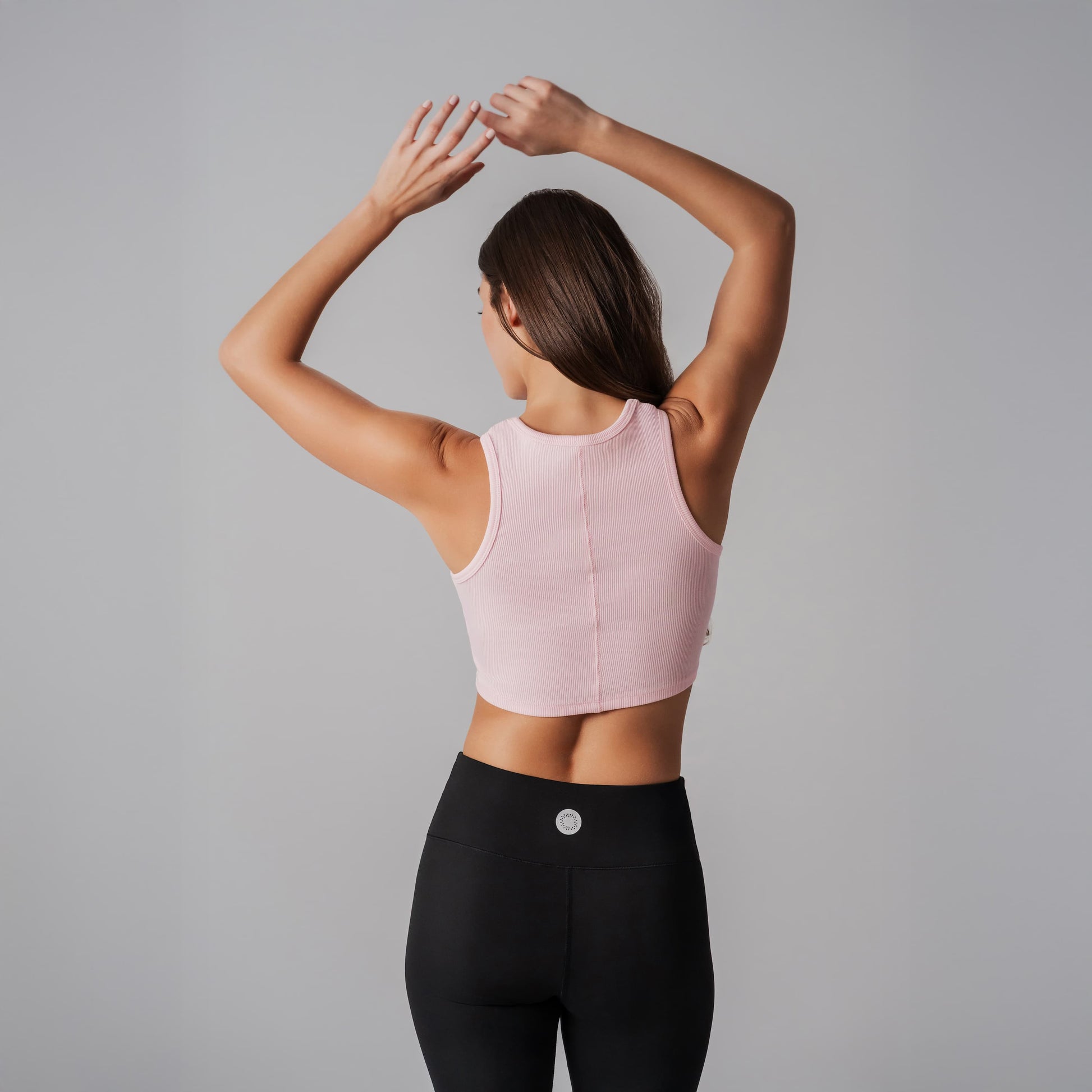 Woman wearing a pink tank bra and black leggings against a gray background