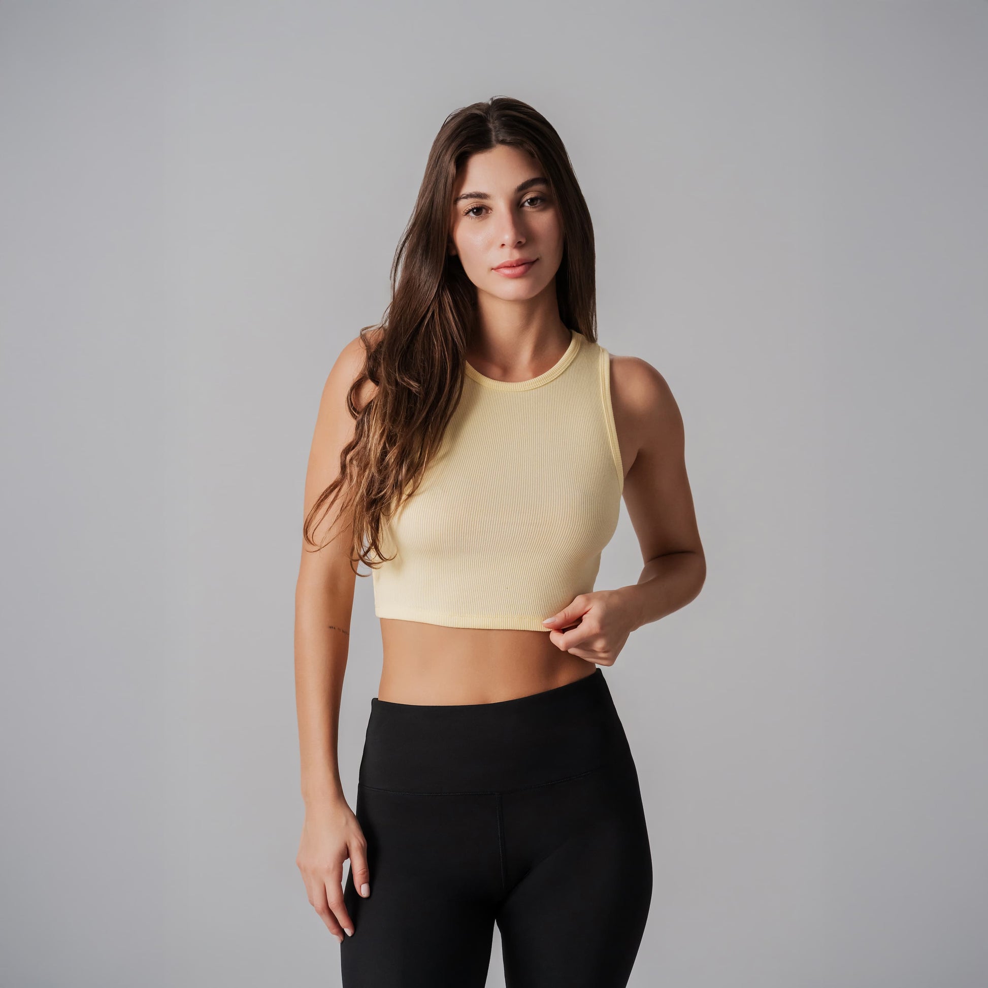 Woman wearing a yellow sports bra and black leggings on a gray background