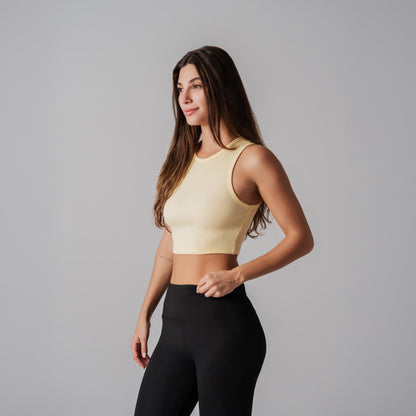 Woman wearing a light yellow sports bra and black leggings on a gray background