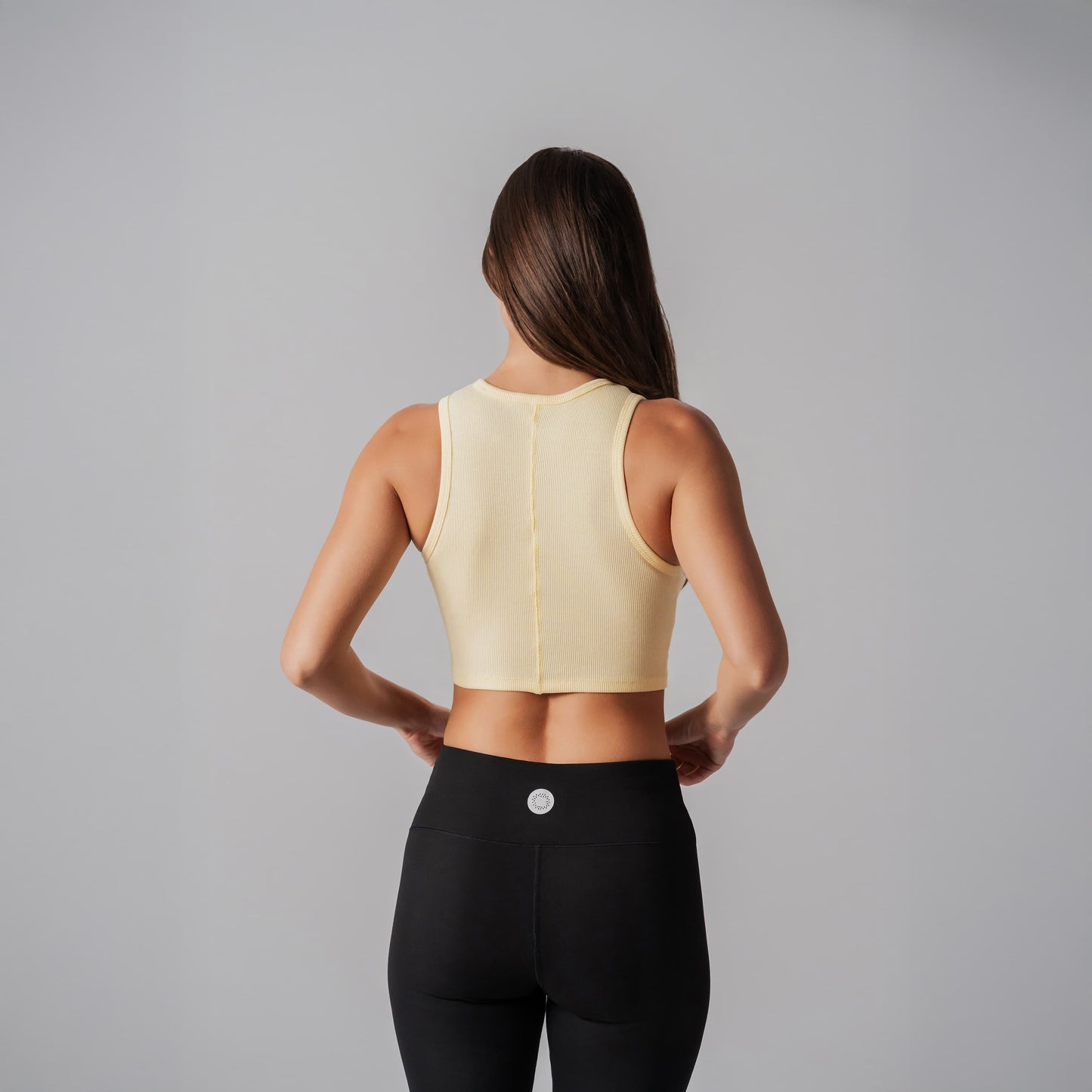 Person wearing a light yellow sports bra and black leggings on a gray background