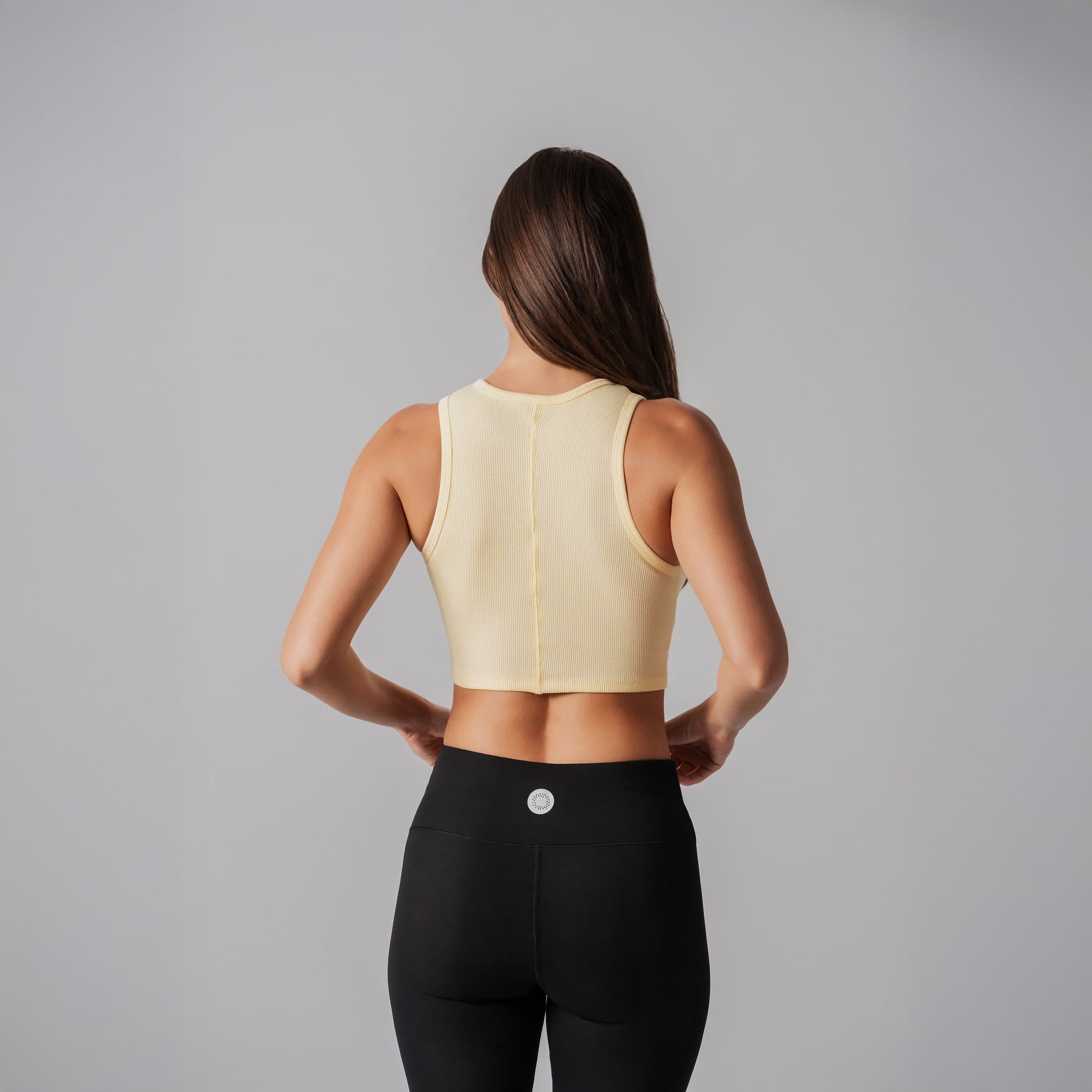 Person wearing a light yellow sports bra and black leggings on a gray background