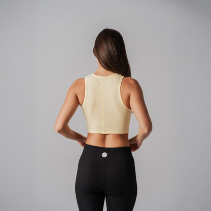 Person wearing a light yellow sports bra and black leggings on a gray background