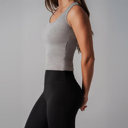 Person wearing a gray tank top and black leggings on a plain background