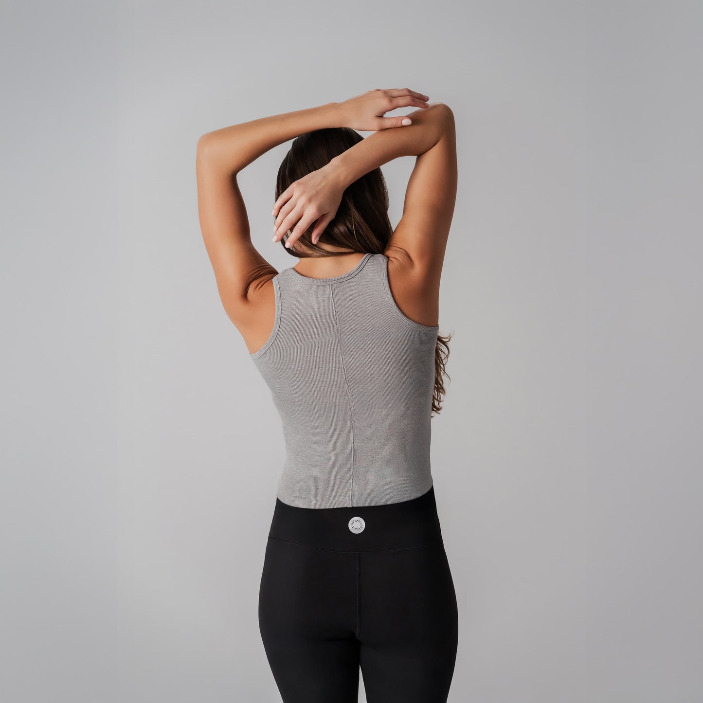 A model wearing a gray tank top and black leggings against a plain background