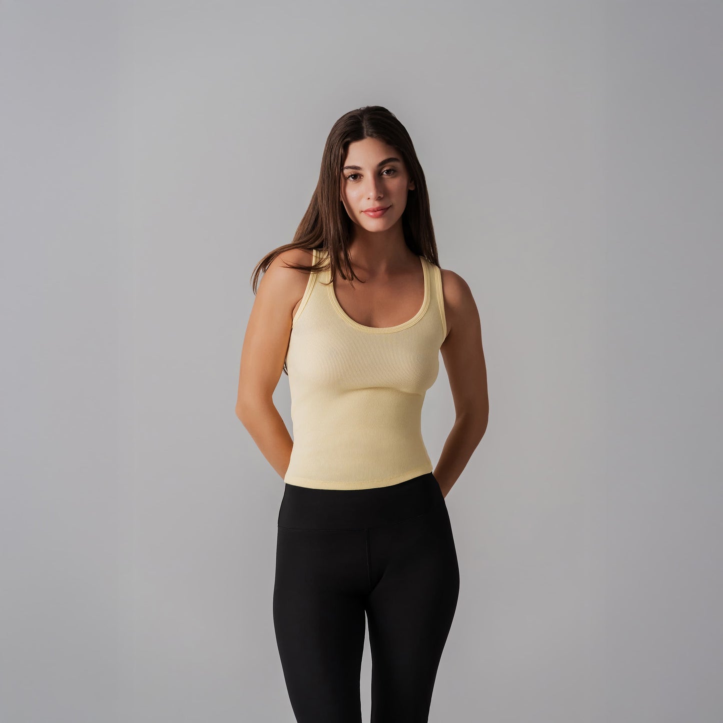 Woman wearing a yellow tank top and black leggings against a gray background