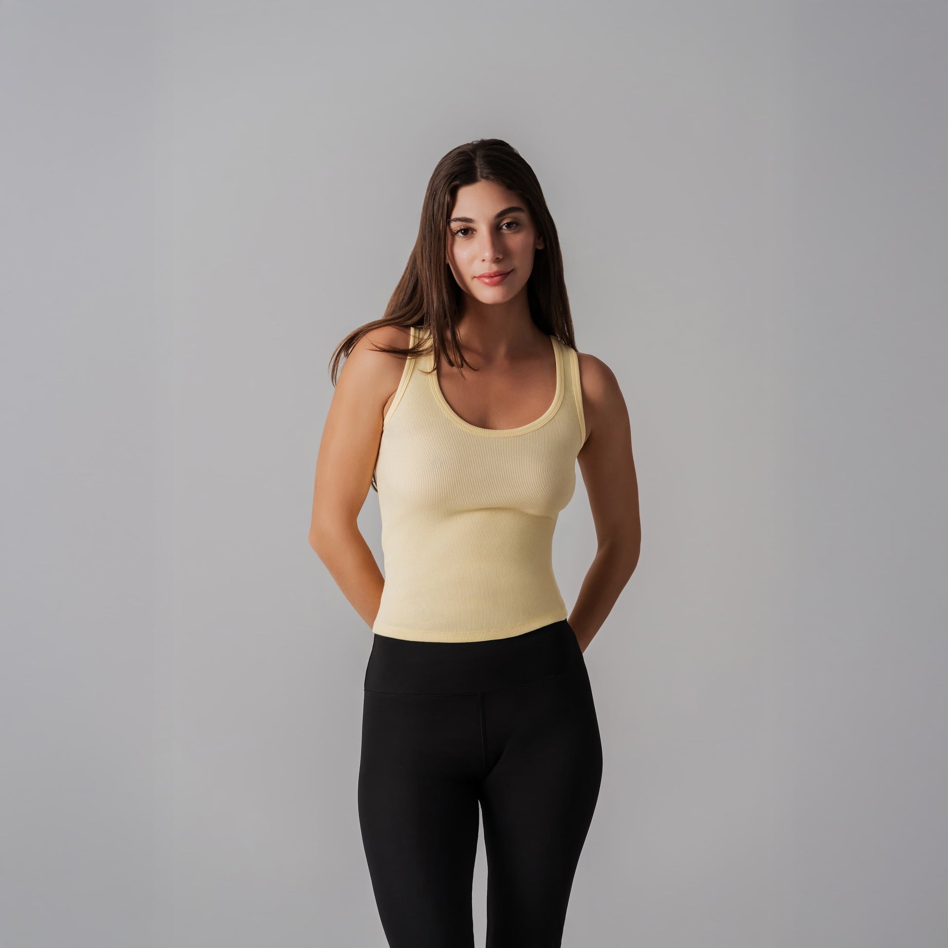 Woman wearing a yellow tank top and black leggings against a gray background