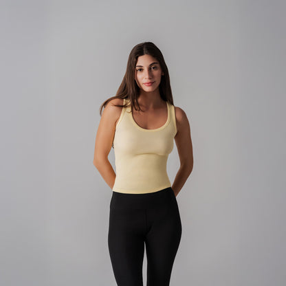 Woman wearing a yellow tank top and black leggings against a gray background